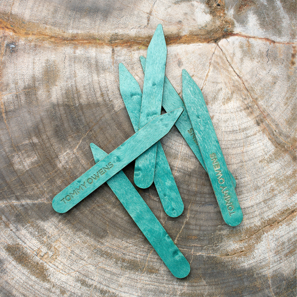 Turquoise birdseye maple collar stays scattered on a piece of turquoise fabric, highlighting their unique color and delicate pattern.