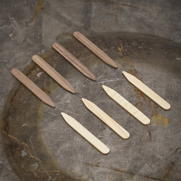 Two-tone ash and walnut collar stays arranged side-by-side, emphasizing the contrast between the light and dark wood tones.